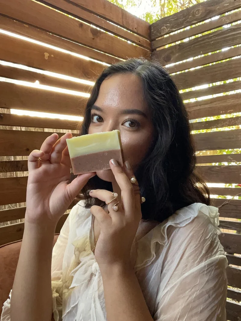 A tan skinned person holds a two-toned facial bar in front of her face