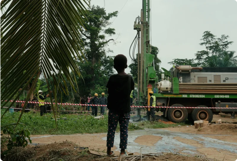 A child stands watching a drilling rig begin to drill for clean water in a community in Sierra Leone.