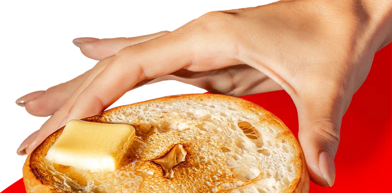 HAND HOLDING A BETTER BAGEL WITH BUTTER ON TO