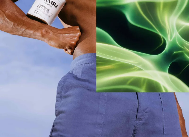 Close-up of a person’s arm and torso holding a white ARMRA colostrum container, wearing blue shorts under a clear blue sky.
