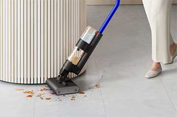 A user cleaning around the edges of a curved kitchen island with the Dyson WashG1 wet cleaner