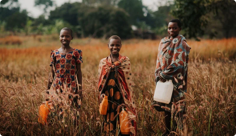 Three girls smile at the camera while holding jerry cans.