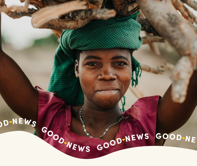 A girl smiles at the camera while carrying branches above her head.