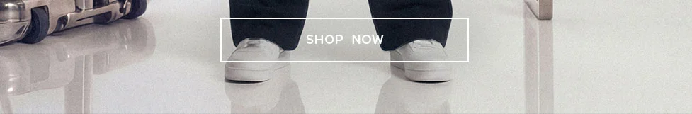 Person in dark pants and crisp white sneakers stands on a reflective surface, promoting new arrivals in casual footwear. Shop Now!
