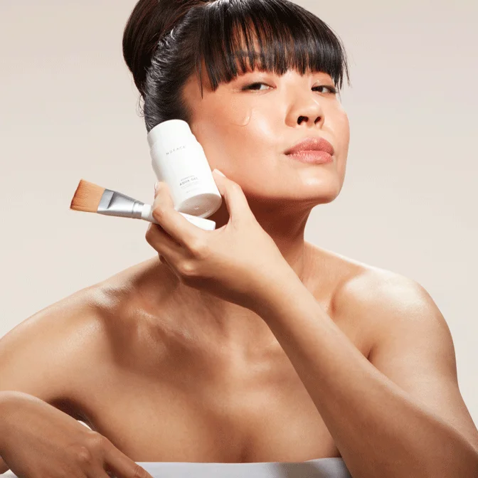 Woman holding Clean Sweep Brush and Hydrating Aqual Gel to her cheek bone.