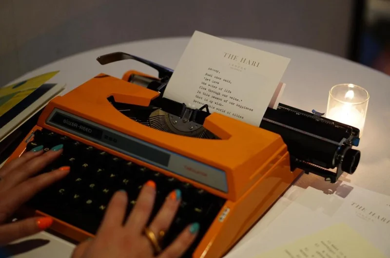 Hands typing a poem on an orange typewriter
