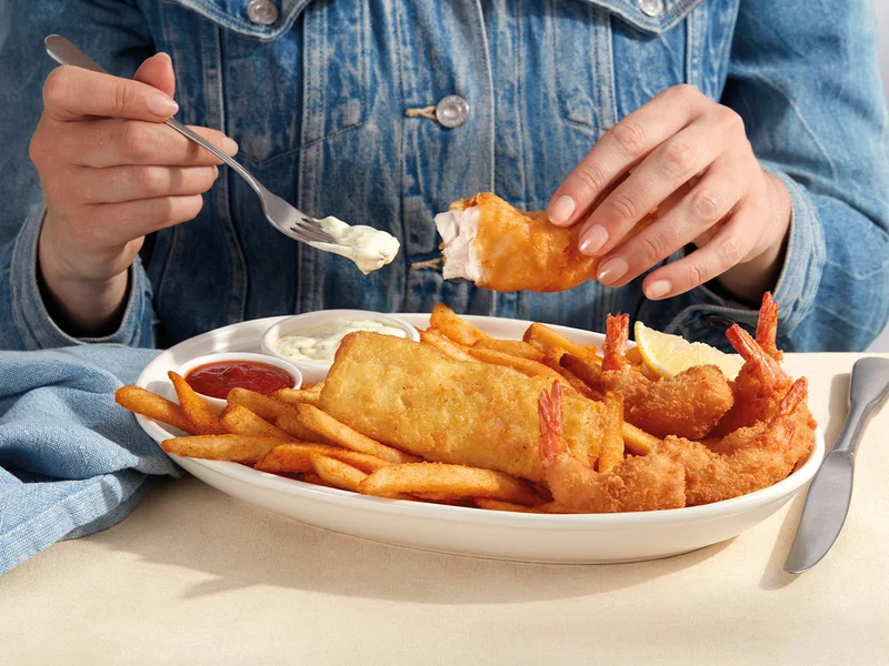 A person in a denim buttoned shirt eats the Fisherman’s Platter with a fork.