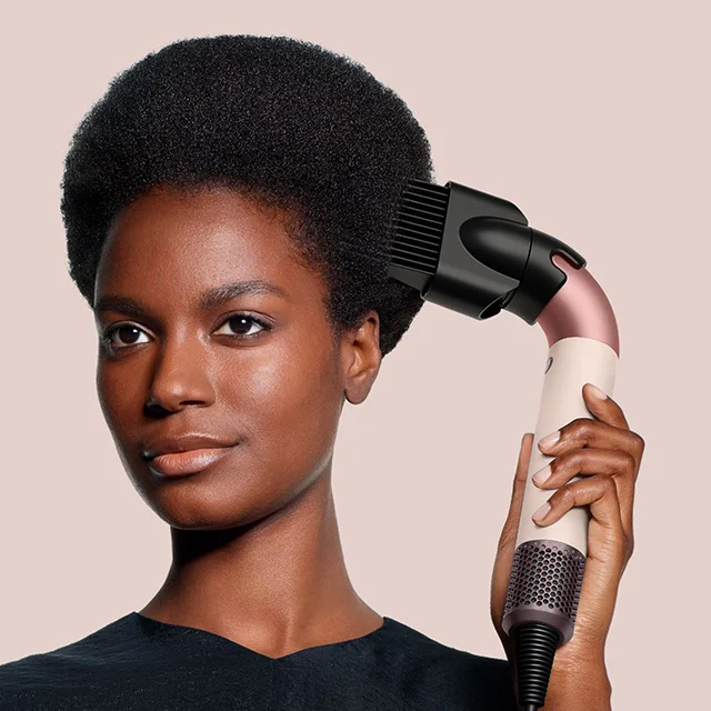 Model holds the Dyson Supersonic r hair dryer in Ceramic pink and rose gold