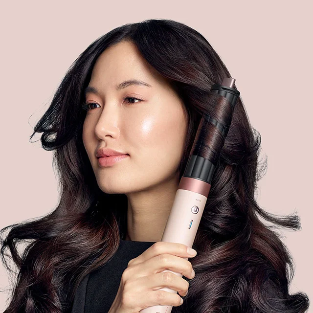 Model styles her hair with the Dyson Airwrap Co-anda2x multi-styler and dryer in Ceramic pink and rose gold