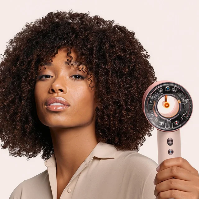 Model holds the Dyson Supersonic Nural hair dryer in Ceramic pink and rose gold