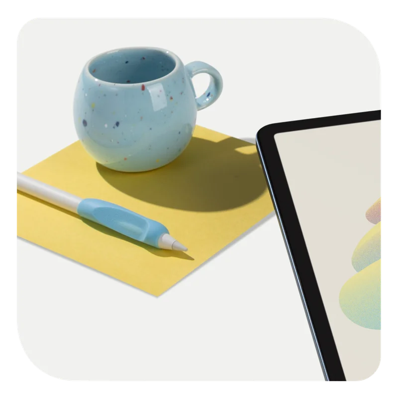 An Apple Pencil with Paperlike's Pencil Grip (2nd Generation) in Paperlike Blue sitting on top of a square yellow piece of paper next to a blue speckled mug. An iPad sits in the lower right corner.