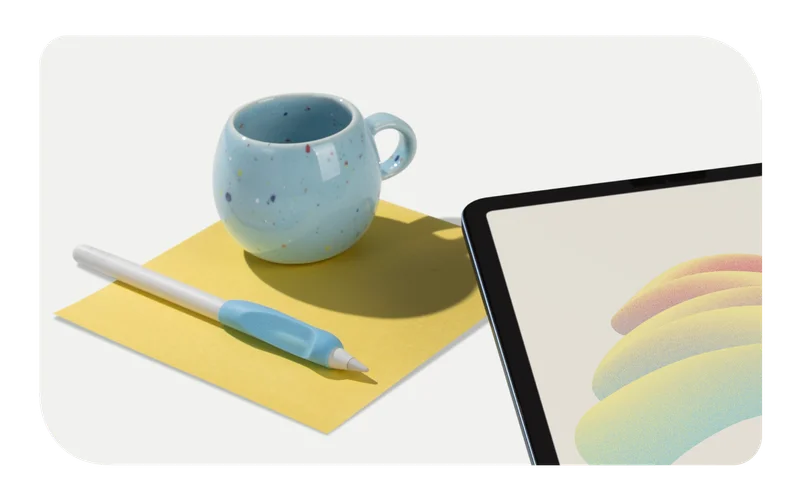 An Apple Pencil with Paperlike's Pencil Grip (2nd Generation) in Paperlike Blue sitting on top of a square yellow piece of paper next to a blue speckled mug. An iPad sits in the lower right corner.