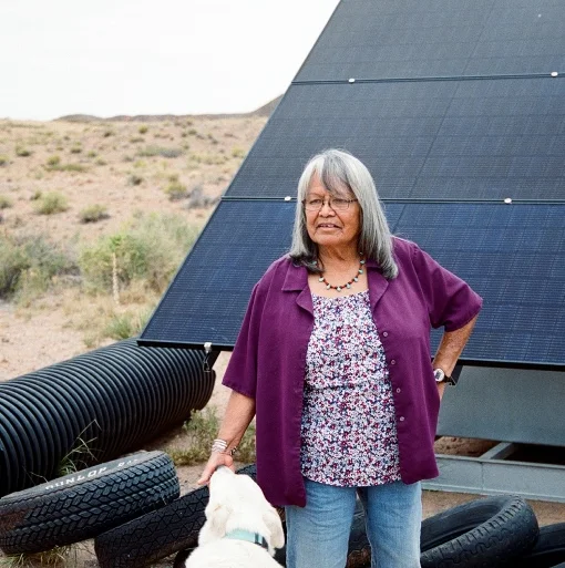 A person and dog stand in front of a solar panel rack.
