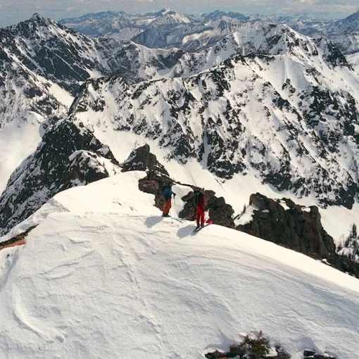 Two skiers stand on the summit of a mountain.