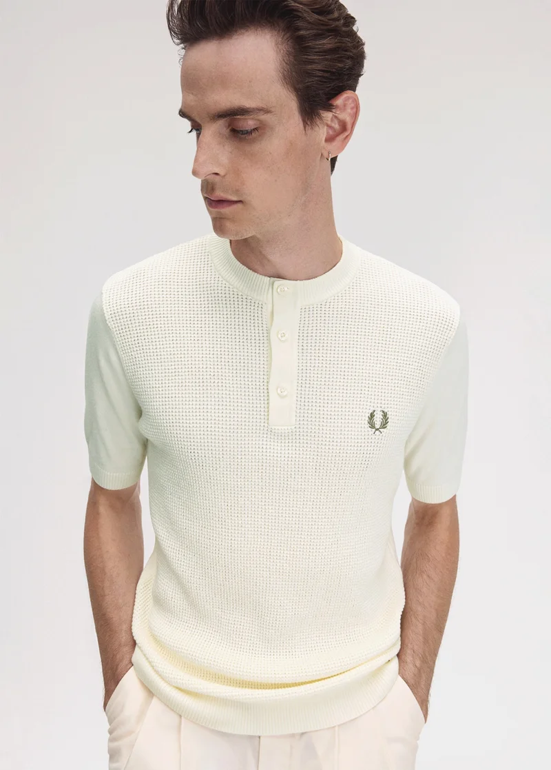 Fred Perry New Releases: white model with blue eyes and slicked back dark hair wears a Light Ecru Waffle Stitch Henley Shirt