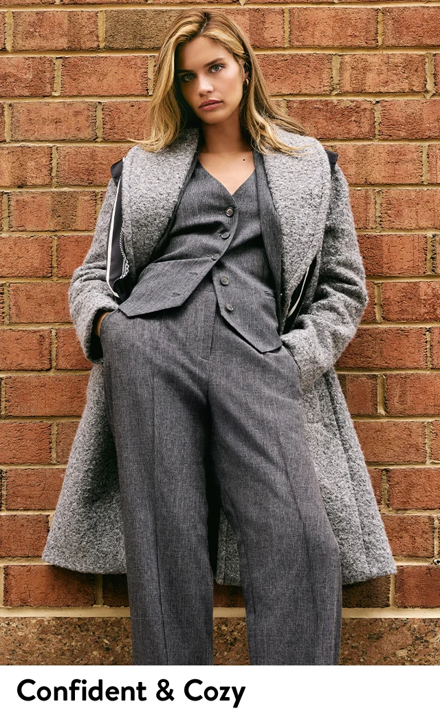 A woman wearing a grey overcoat, grey vest and grey trousers.