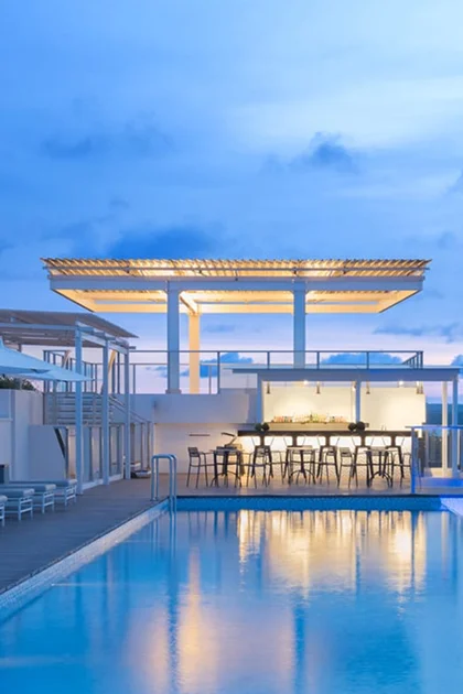 A pool just after sunset with a lit seating area and covered patio at one end.
