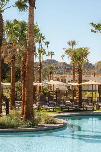 A resort with a winding pool surrounded by palm trees with large hills in the background.