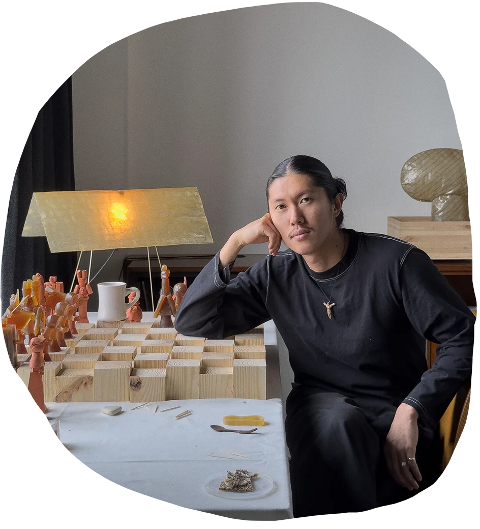 Minjae Kim wearing all black rests his elbow on a handmade wooden chess board