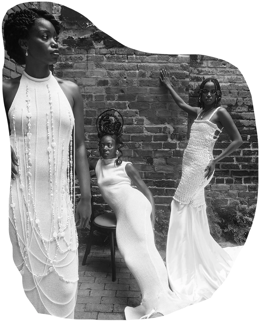 Three women stand in a brick courtyard, wearing intricately knitted white wedding gowns by