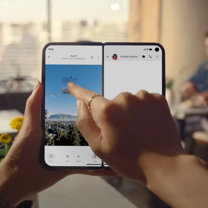 A person holds a foldable phone and drags a photo from one screen to a message on the other screen.