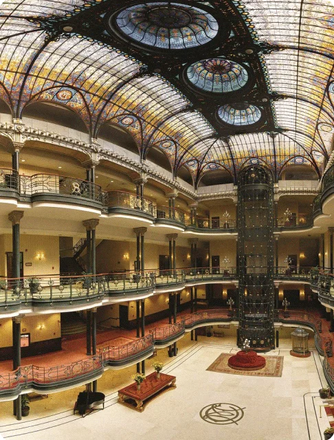 Image Description: The fabulous Art Nouveau-style interiors of the Gran Hotel Ciudad De Mexico lobby, with stained glass ceilings and a gilded open elevator