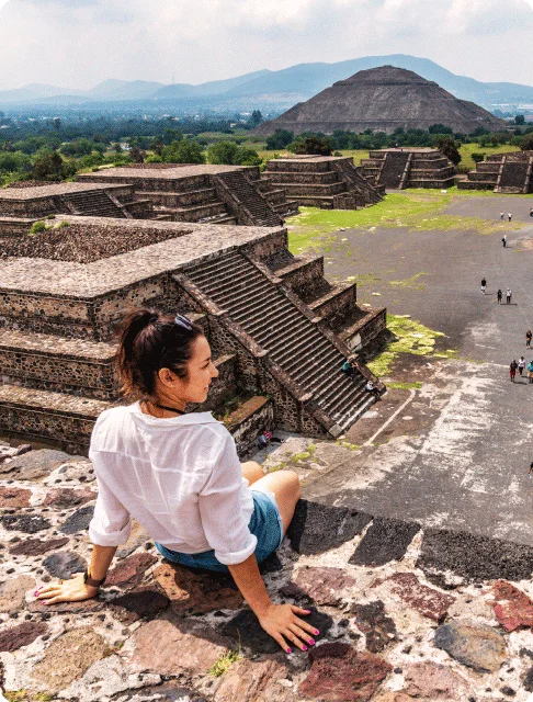 Image Description: A seated traveler admires a view of the Teotihuacan Pyramids, including the Pyramid of the Sun