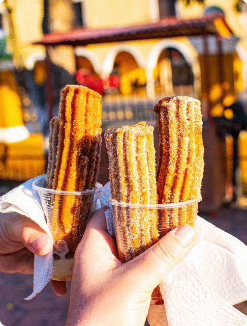 Image Description: A close-up of travelers holding two cups of churros together on a street in Mexico City