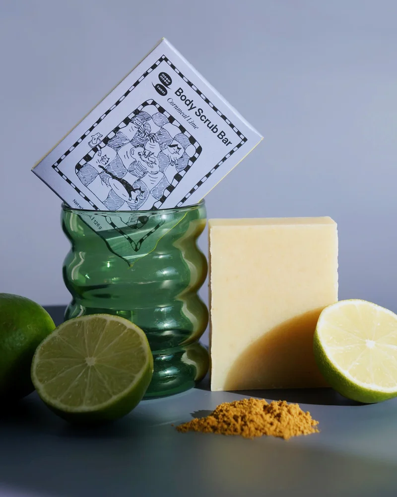 A white bar of soap sits next to a green glass that a blue box is propped in