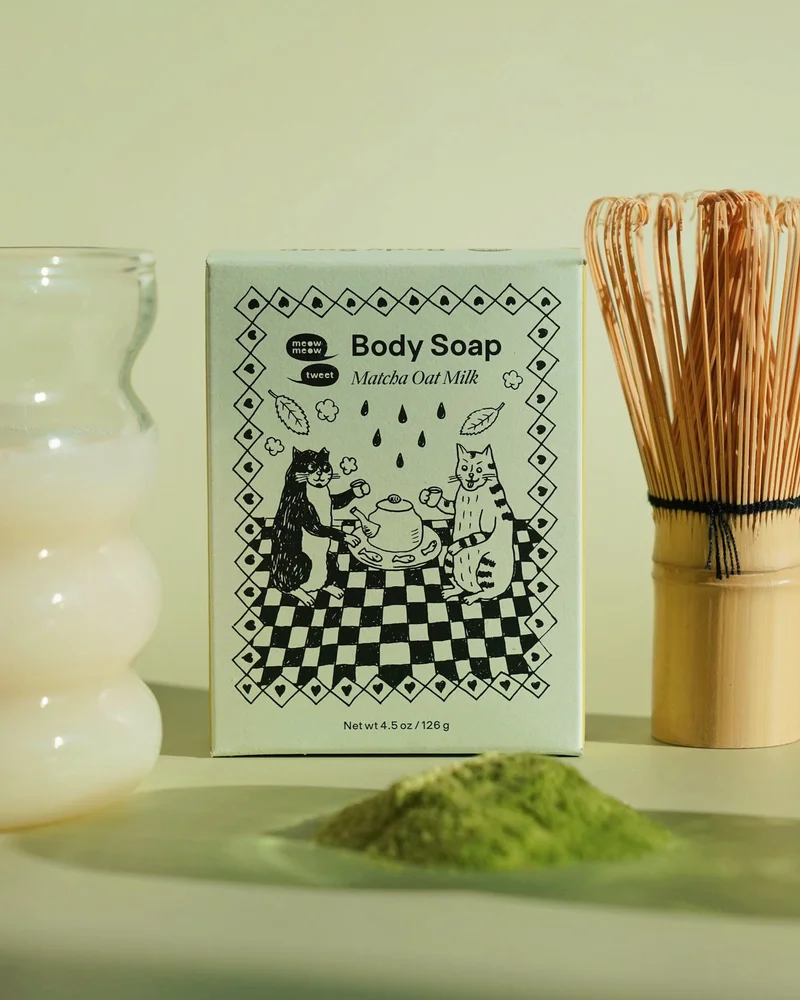A light green soap box sits between a matcha brush and a glass of oat milk