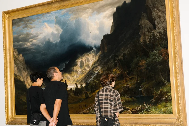 Three people looking at Albert Bierstadt’s “A Storm in the Rocky Mountains, Mt. Rosalie”
