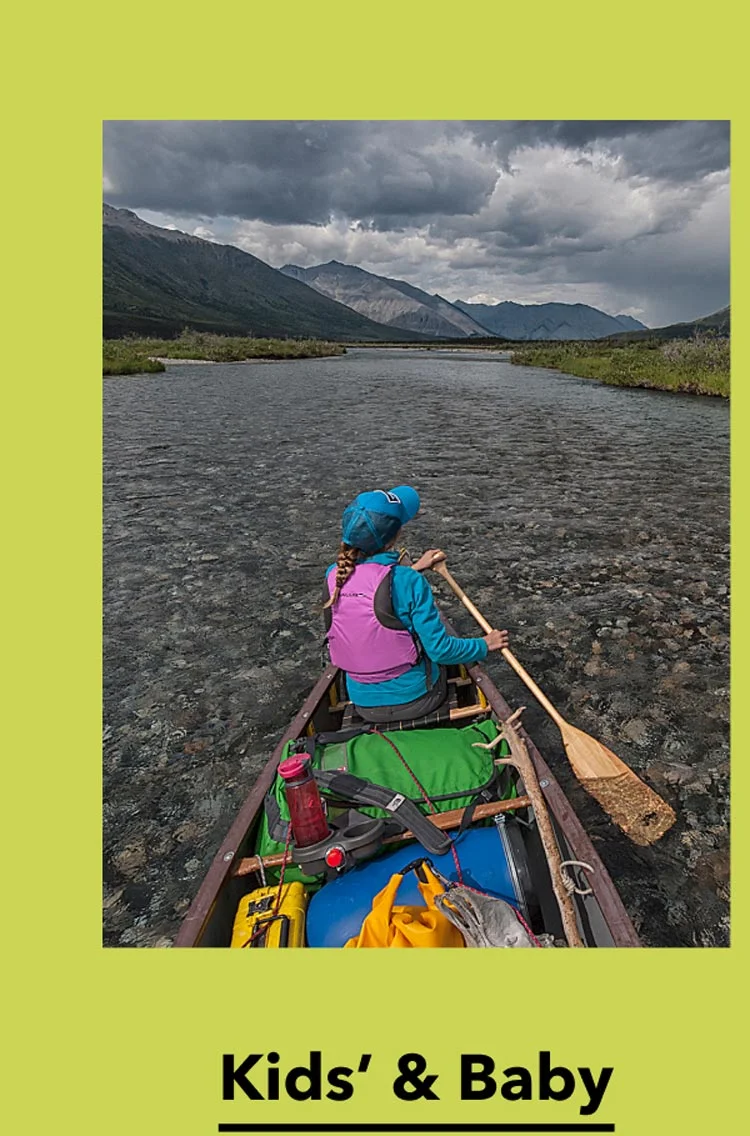 A canoeist paddles a clear river beneath storm clouds.