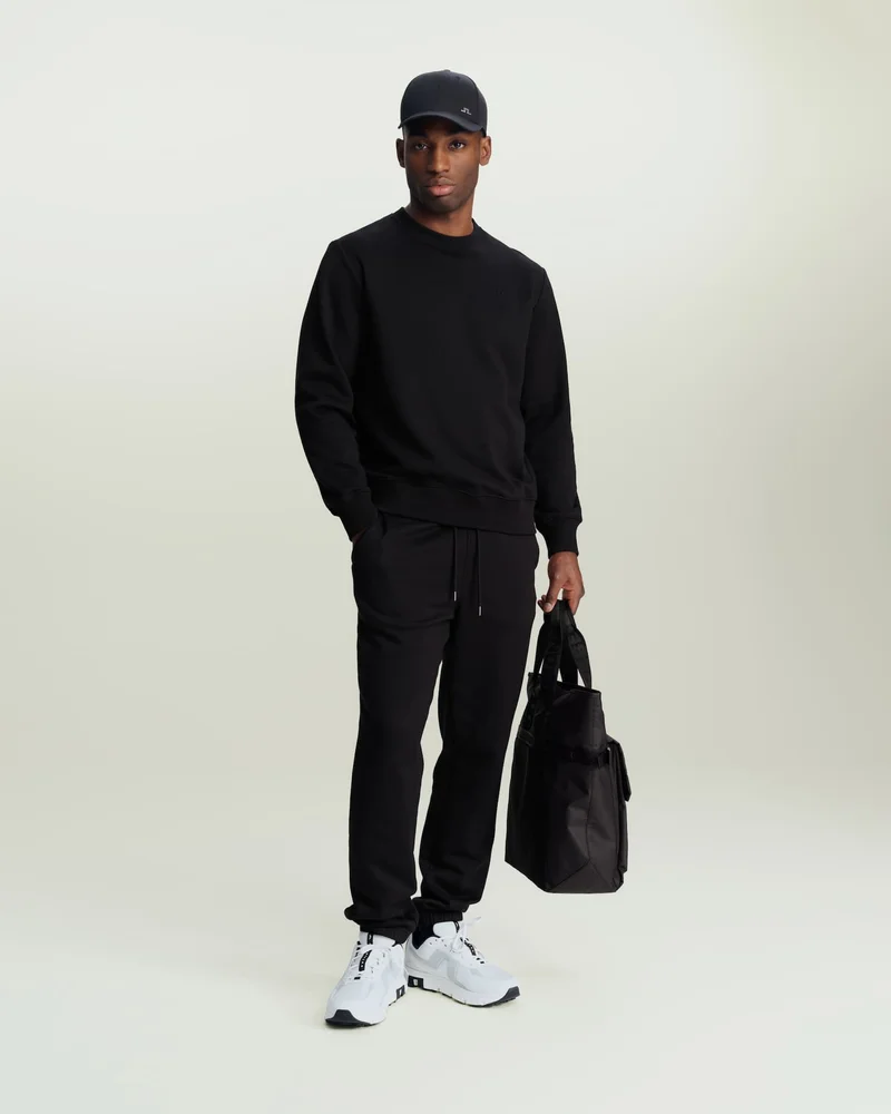 an image of a man in a black sweatshirt and sweatpants holding a bag