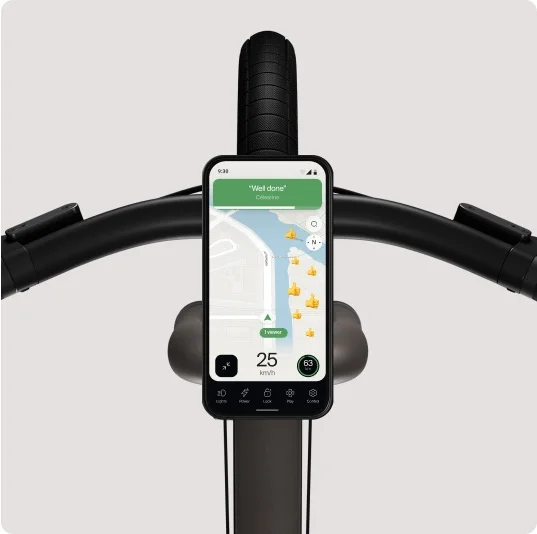 A render showing a smartphone mounted on the handlebars of a Cowboy e-bike, displaying the speed with an “Adaptive” mode indicator on the screen.