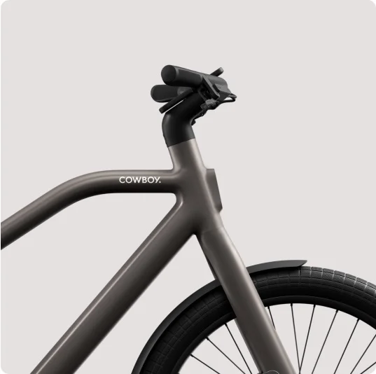 A render. a Cowboy e-bike frame, showing a minimalist design with a black saddle and sand-coloured frame.
