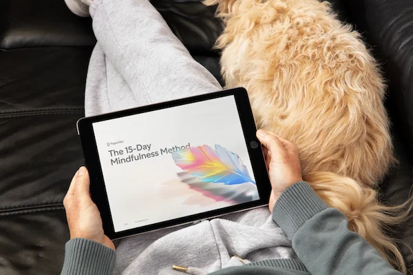 A person lying on a couch with their dog, holding an iPad with the 15-Day Mindfulness Method journal by Paperlike open on the screen.
