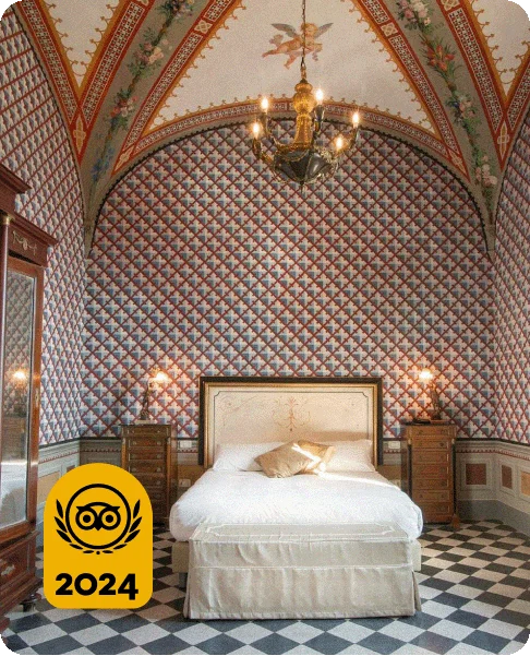 Image Description: A white bed in the middle of a room with blue and white checkered floors and red, white, and blue tile walls and a mosaic of a cherub and flowers. An opulent chandelier hangs from the ceiling. A gold 2024 Travelers’ Choice Awards Best of the Best badge is on the bottom left corner of the image.
