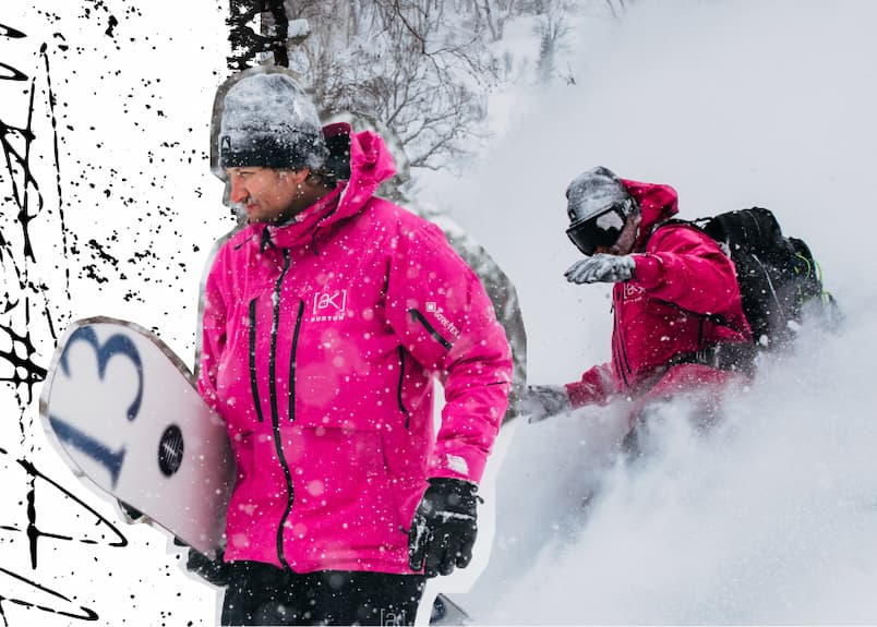 The Men's [ak]® Hover GORE‑TEX C-KNIT 3L Stretch Jacket in Very Berry on a rider carrying a the Burton Family Tree Hometown Hero snowboard. In the background, he is riding powder.