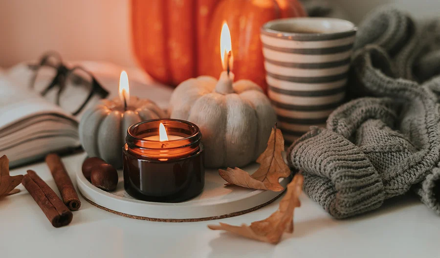 A table with lit candles, small pumpkins, and a book, evoking a warm, seasonal ambiance.