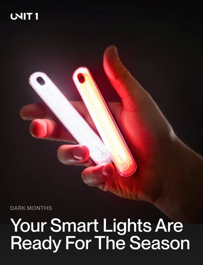 Hand holding UNIT 1 Smart Lights, showing red and white beams, ready for fall riding.