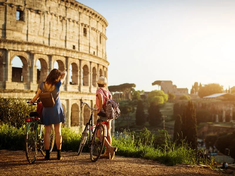 Two tourists standing by bicycles in front of the Colosseum, Rome, Italy.