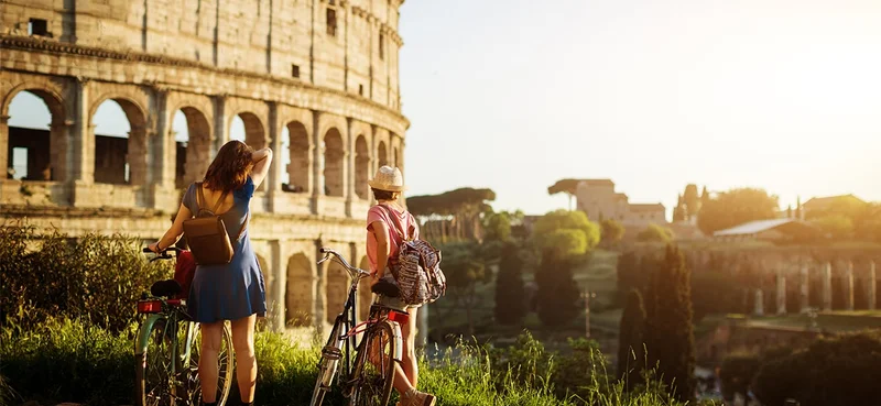Two tourists standing by bicycles in front of the Colosseum, Rome, Italy.