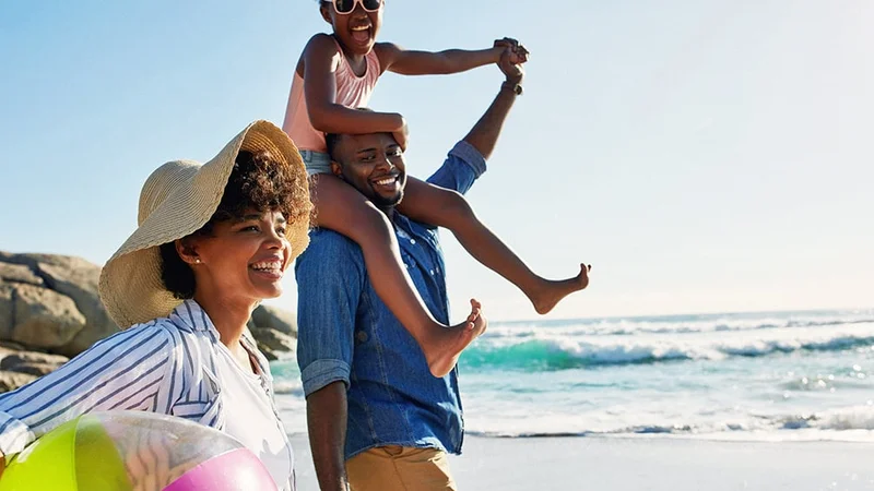 Image description: Family of three walking on the beach on a sunny day