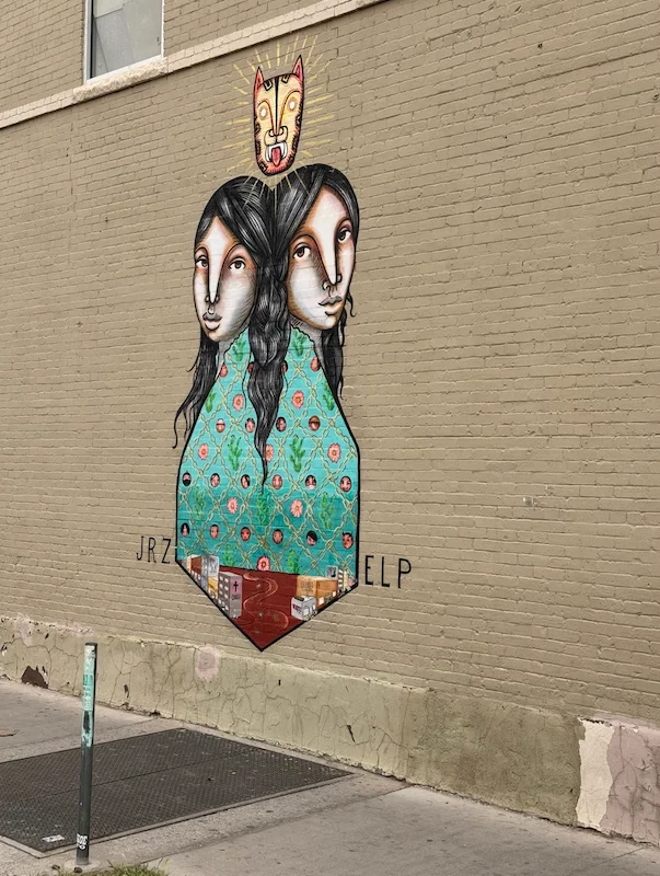 A photo of a mural depicting two women standing back-to-back with a tiger head over them
