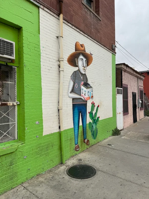 A photograph of a mural depicting a man holding a house next to cactus