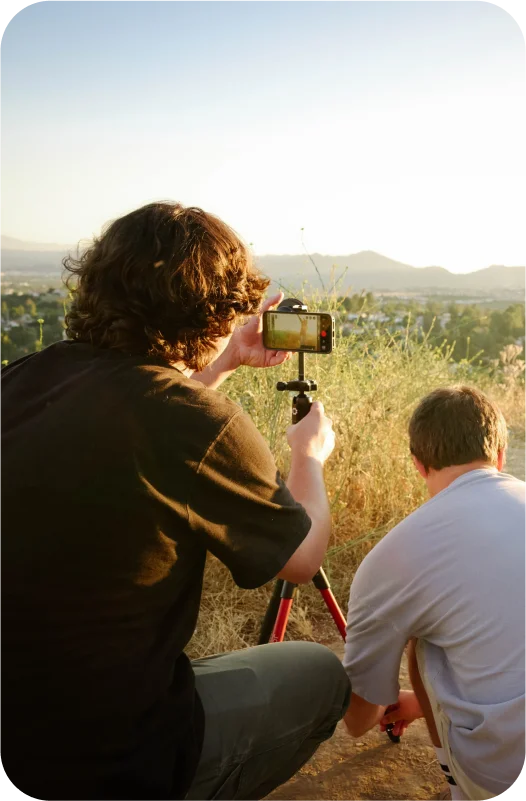 Two men on a hill with a phone shooting photos