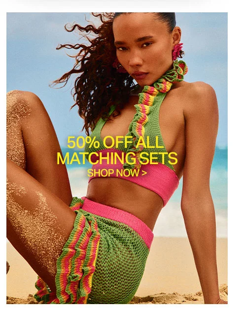 Woman on beach in green crochet matching set with pink/yellow trim. Promoting 50% off all matching sets, ideal for summer beachwear.
