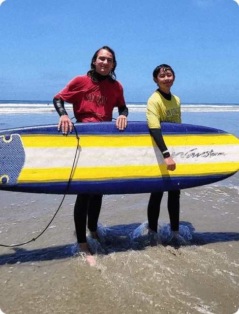 Image Description: An adult and child traveler holding up a surfboard together