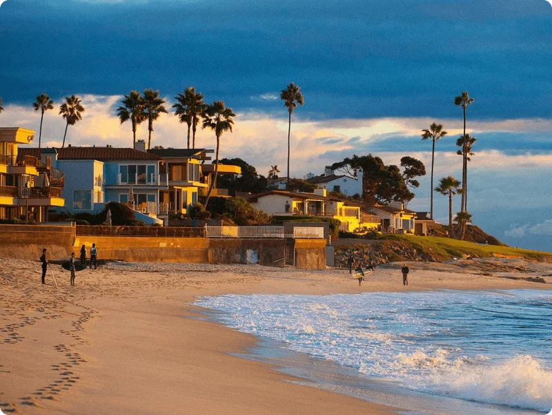 Image Description: A view of travelers and surfers enjoying the sunset along Marine Street Beach in San Diego, with palm trees in the background