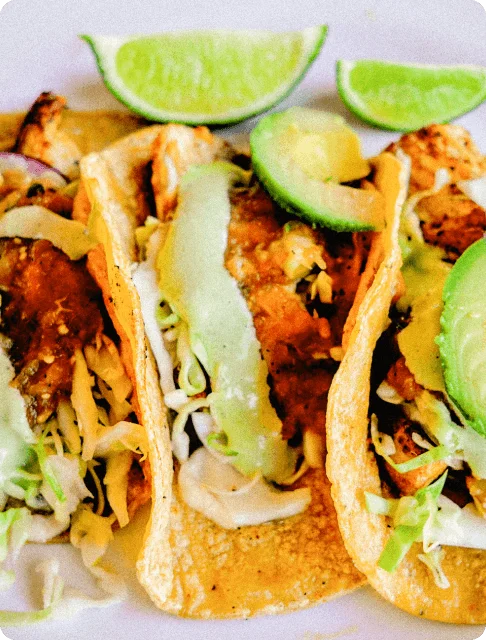 Image Description: A close-up of fried fish tacos garnished with avocado cilantro sauce and lime slices at the side